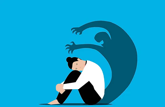 Person sitting with knees held close while a large shadow looms behind, symbolizing the emotional weight of low self-esteem and negative self-perception.